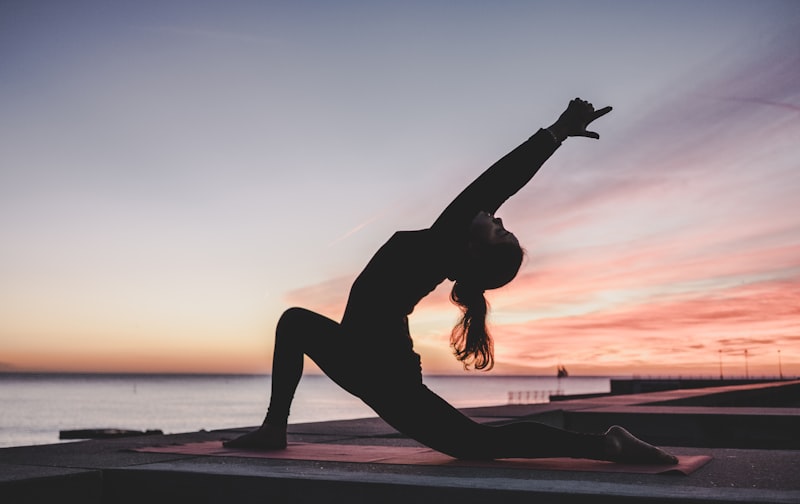 Silhouette einer Person in einer Yoga-Ausfallschritt-Pose am Meer bei Sonnenuntergang